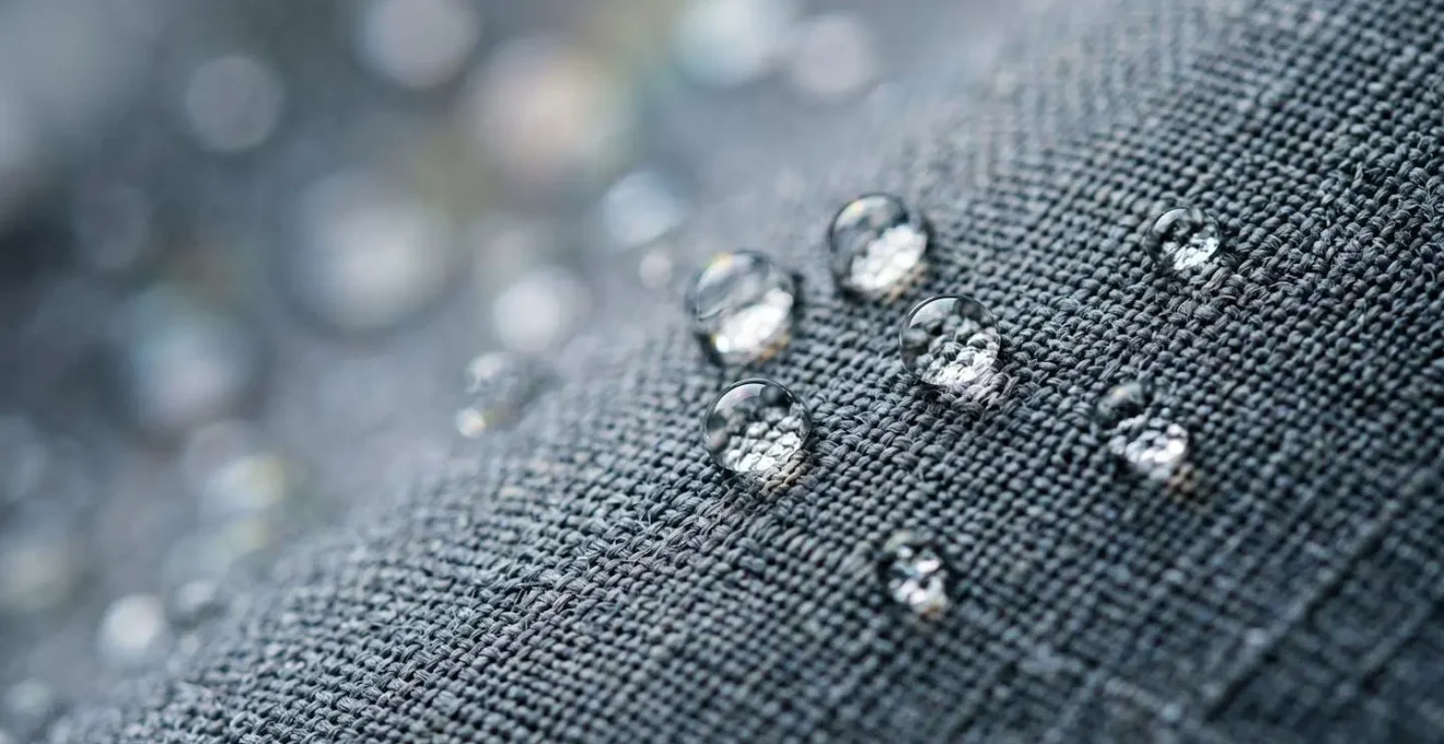 Extreme close-up of water droplets beading on technical waterproof fabric surface showing breathable membrane texture